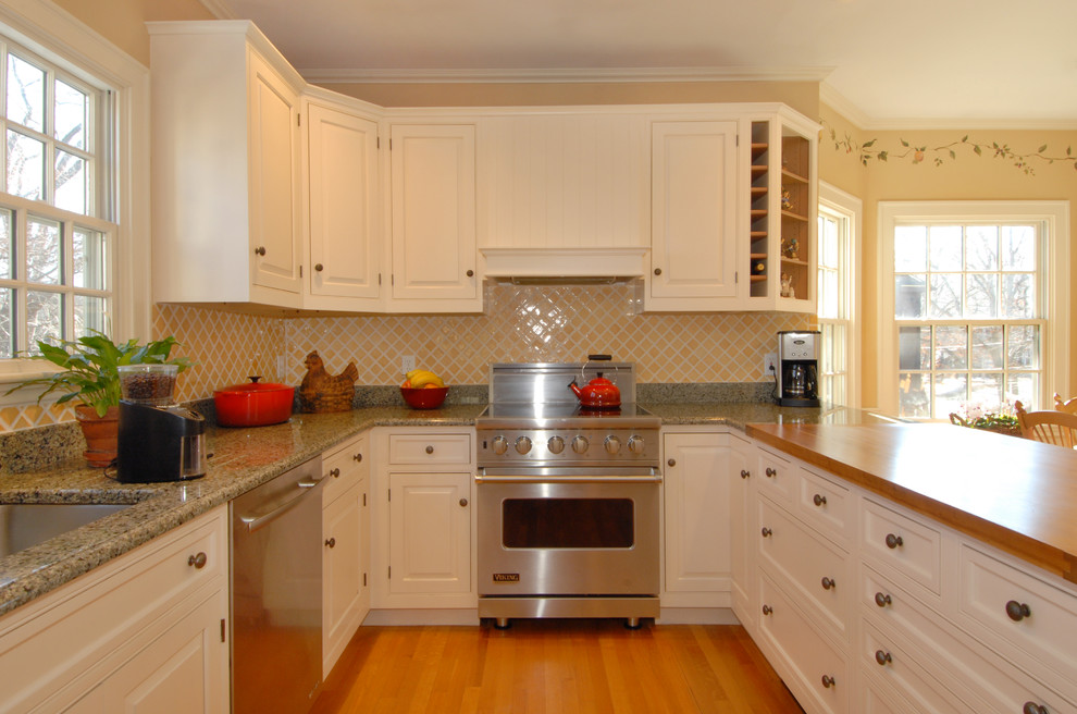Klassisk inredning av ett stort u-kök, med granitbänkskiva, gult stänkskydd, stänkskydd i porslinskakel, rostfria vitvaror, mellanmörkt trägolv, en köksö, vita skåp och luckor med profilerade fronter