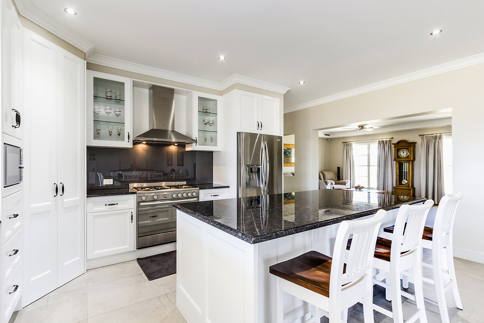 Klassische Küche mit Schrankfronten mit vertiefter Füllung, weißen Schränken, Küchenrückwand in Schwarz, Küchengeräten aus Edelstahl und Kücheninsel in Hobart