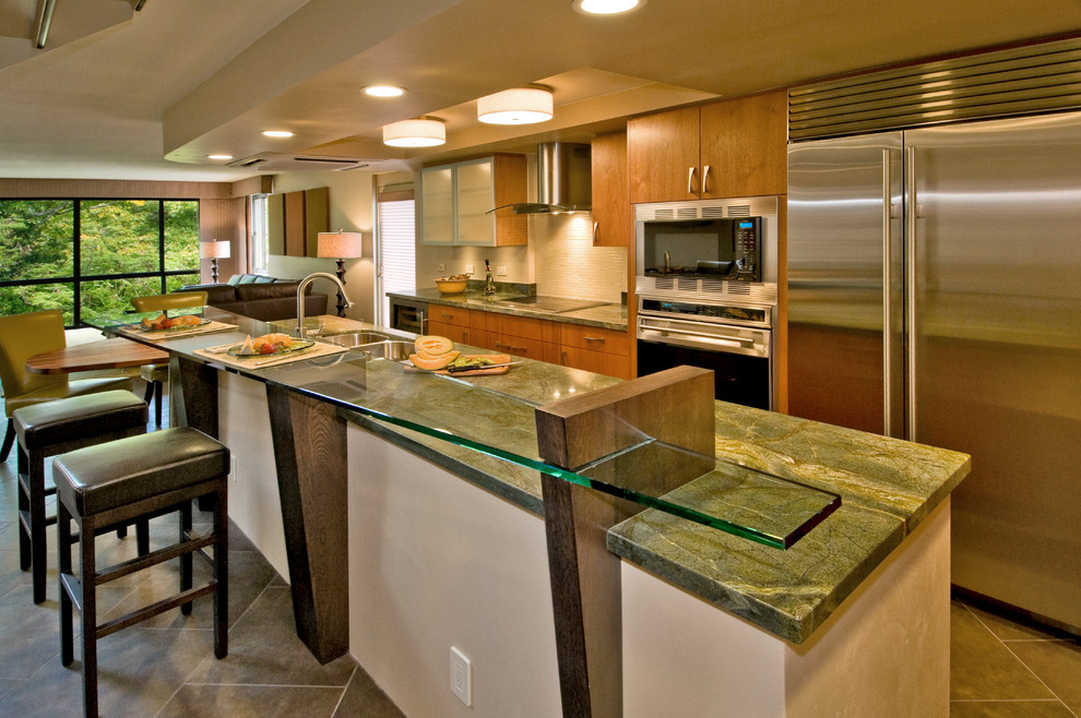 Foto på ett stort tropiskt grön l-kök, med en undermonterad diskho, släta luckor, skåp i mellenmörkt trä, granitbänkskiva, beige stänkskydd, stänkskydd i stenkakel, rostfria vitvaror, skiffergolv, en köksö och grått golv