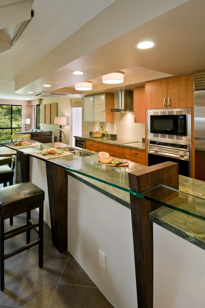 ハワイにある広いトロピカルスタイルのおしゃれなキッチン (シルバーの調理設備、スレートの床、グレーの床、アンダーカウンターシンク、フラットパネル扉のキャビネット、中間色木目調キャビネット、御影石カウンター、ベージュキッチンパネル、石タイルのキッチンパネル) の写真