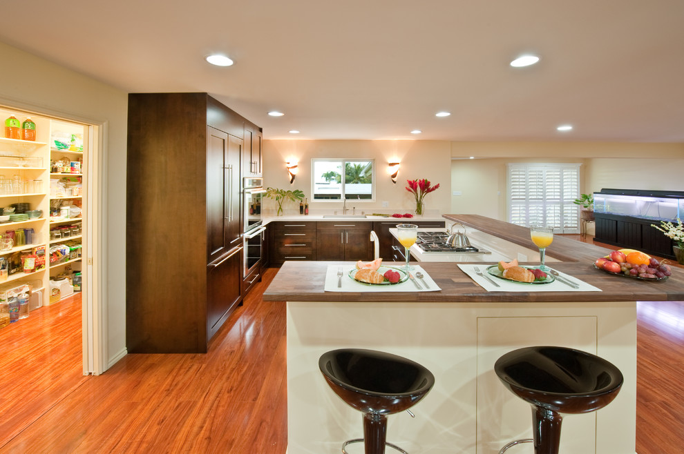 Foto på ett stort tropiskt l-kök, med en undermonterad diskho, skåp i shakerstil, skåp i mörkt trä, bänkskiva i koppar, vitt stänkskydd, integrerade vitvaror, mellanmörkt trägolv och brunt golv