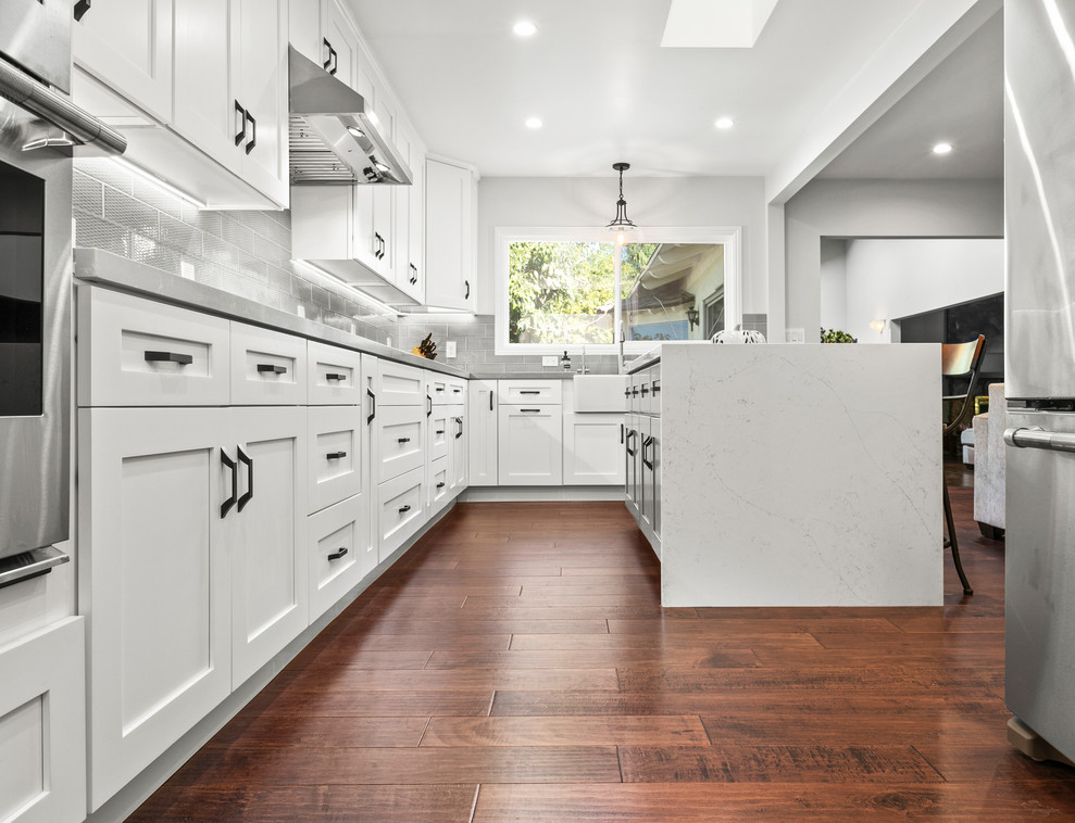 Large classic kitchen/diner in Los Angeles with shaker cabinets, white cabinets, engineered stone countertops, grey splashback, porcelain splashback, stainless steel appliances, medium hardwood flooring, brown floors and grey worktops.