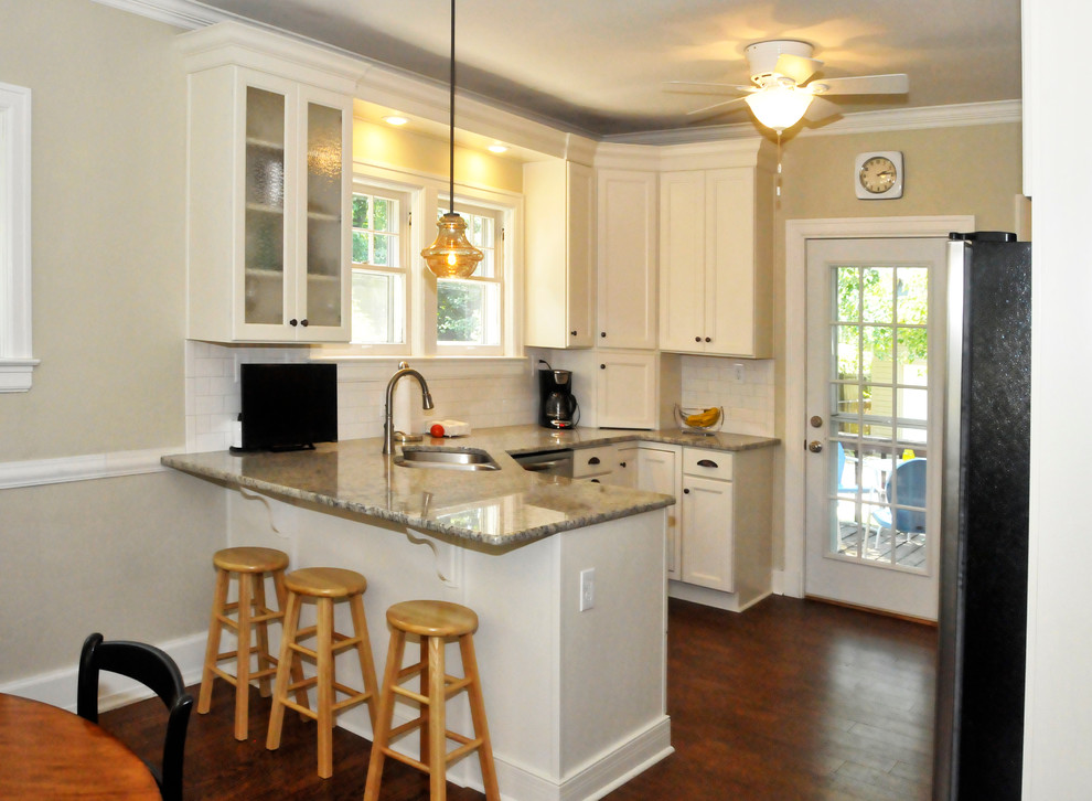 Exempel på ett litet klassiskt kök, med en undermonterad diskho, luckor med infälld panel, vita skåp, granitbänkskiva, vitt stänkskydd, stänkskydd i tunnelbanekakel, rostfria vitvaror, mörkt trägolv, en halv köksö och brunt golv