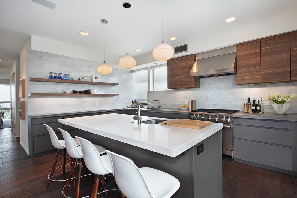 Foto på ett funkis kök med öppen planlösning, med en undermonterad diskho, släta luckor, grå skåp, vitt stänkskydd, rostfria vitvaror, mörkt trägolv och en köksö