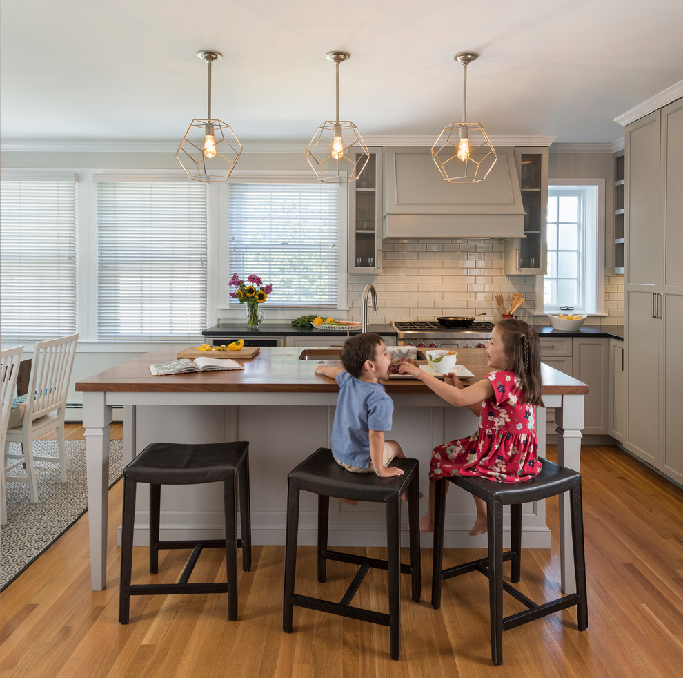 Example of a transitional l-shaped medium tone wood floor eat-in kitchen design in Providence with an undermount sink, shaker cabinets, gray cabinets, white backsplash, subway tile backsplash, stainless steel appliances, an island and black countertops