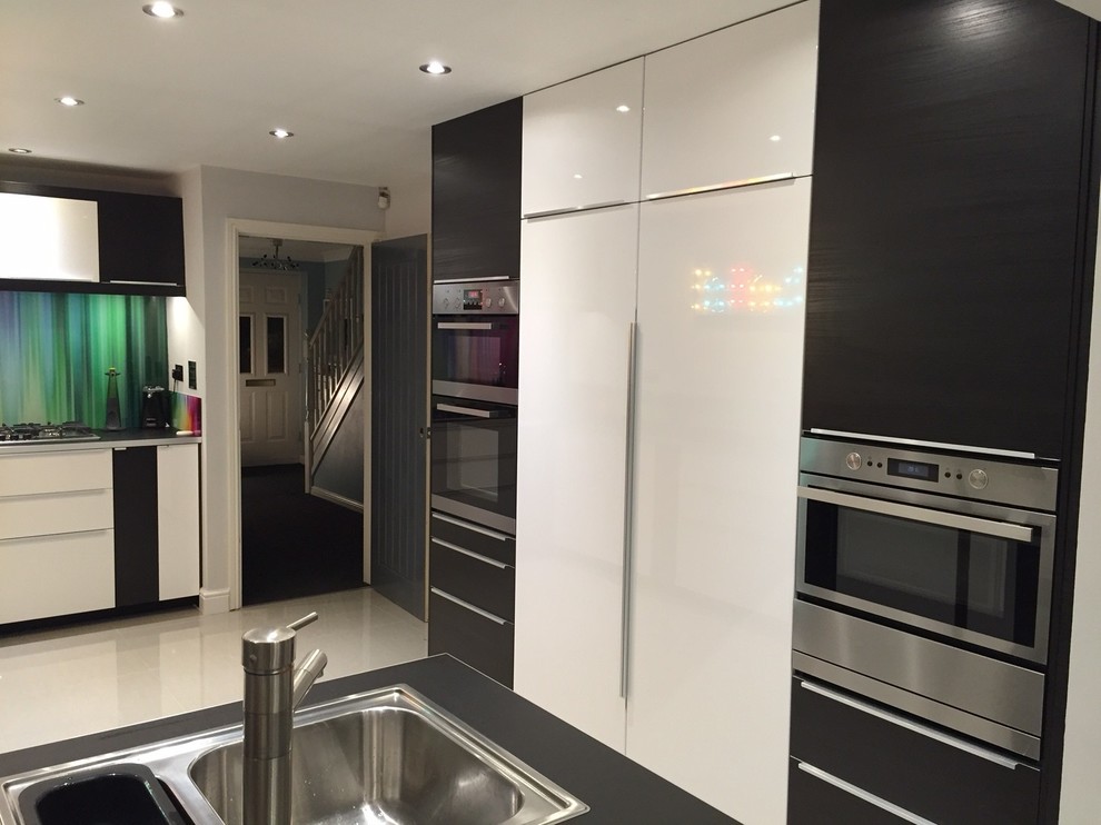 Photo of a large contemporary l-shaped open plan kitchen in Manchester with a single-bowl sink, flat-panel cabinets, white cabinets, laminate countertops, multi-coloured splashback, glass sheet splashback, integrated appliances, porcelain flooring and no island.