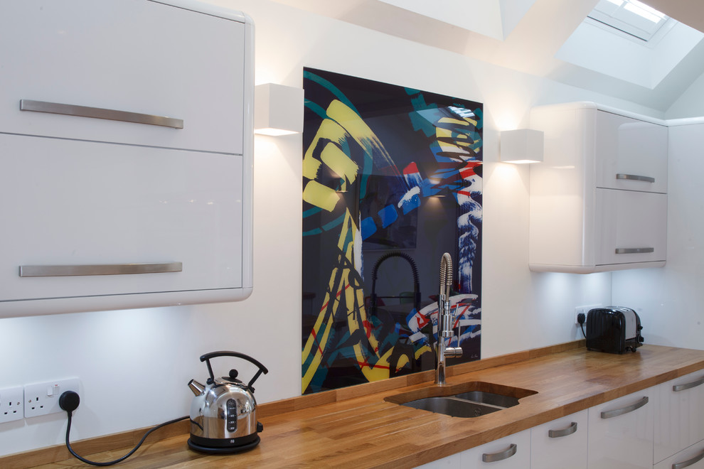 Inspiration for a contemporary kitchen/diner in Cambridgeshire with flat-panel cabinets, white cabinets, wood worktops, multi-coloured splashback and glass sheet splashback.