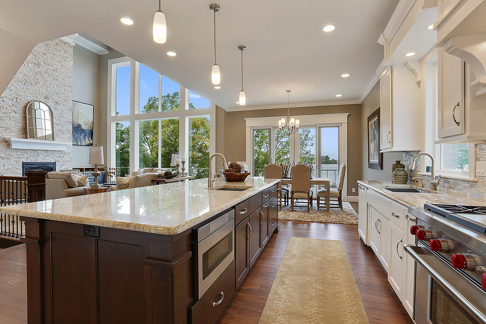 Photo of a large traditional l-shaped kitchen/diner in Other with a built-in sink, raised-panel cabinets, white cabinets, stainless steel appliances, dark hardwood flooring, an island and white splashback.