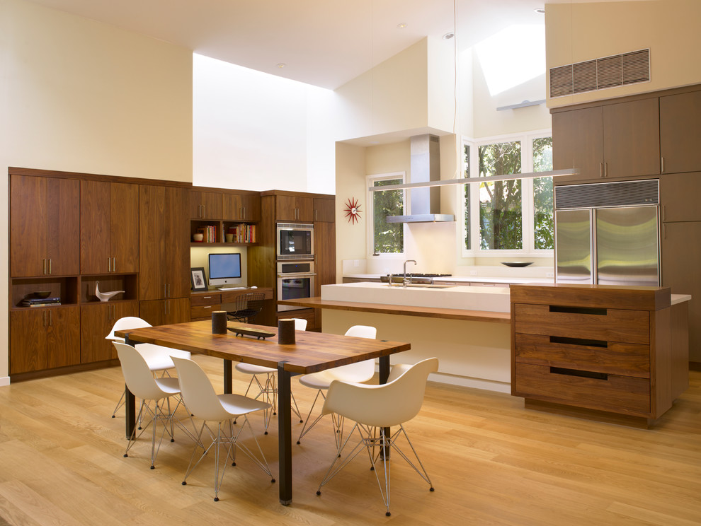 Cette photo montre une cuisine américaine moderne en bois foncé avec un placard à porte plane et un électroménager en acier inoxydable.