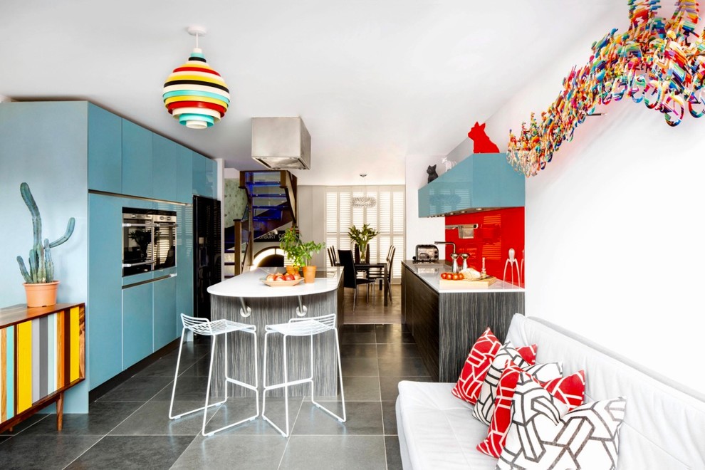 ロンドンにある高級な中くらいなコンテンポラリースタイルのおしゃれなアイランドキッチン (フラットパネル扉のキャビネット、ターコイズのキャビネット、人工大理石カウンター、赤いキッチンパネル、ガラス板のキッチンパネル、セラミックタイルの床、グレーの床) の写真
