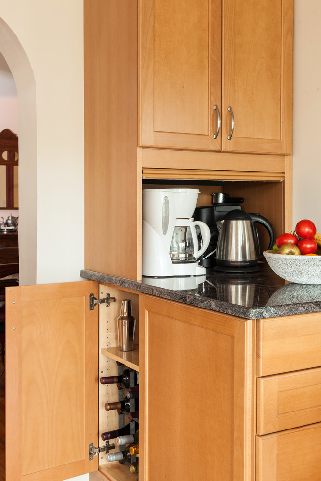 Exemple d'une cuisine américaine chic en L et bois clair de taille moyenne avec un évier encastré, un placard avec porte à panneau encastré, un plan de travail en granite, une crédence beige, une crédence en céramique, un électroménager en acier inoxydable, un sol en liège et îlot.