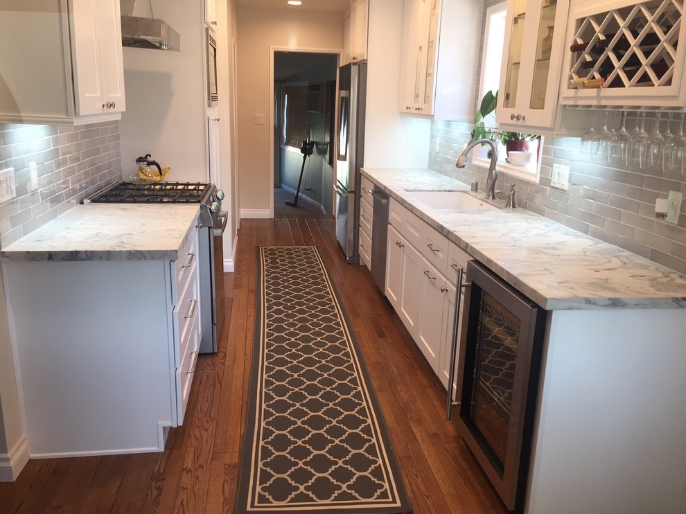 Inspiration for a contemporary medium tone wood floor and brown floor kitchen remodel in Los Angeles with an undermount sink, shaker cabinets, white cabinets, marble countertops, gray backsplash, ceramic backsplash, stainless steel appliances and white countertops
