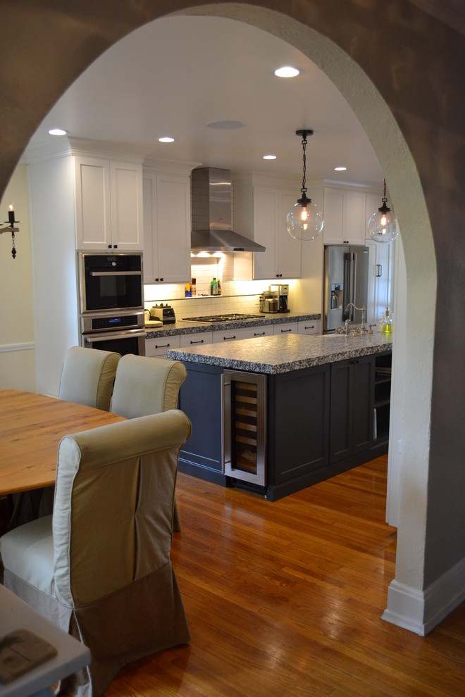 Example of a large transitional galley medium tone wood floor and brown floor eat-in kitchen design in St Louis with a farmhouse sink, granite countertops, white backsplash, subway tile backsplash, stainless steel appliances, an island, white cabinets and shaker cabinets