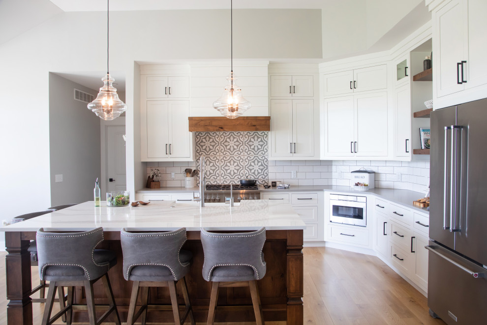 Example of a large cottage l-shaped dark wood floor open concept kitchen design in Milwaukee with a farmhouse sink, flat-panel cabinets, white cabinets, quartz countertops, white backsplash, porcelain backsplash, stainless steel appliances, an island and white countertops