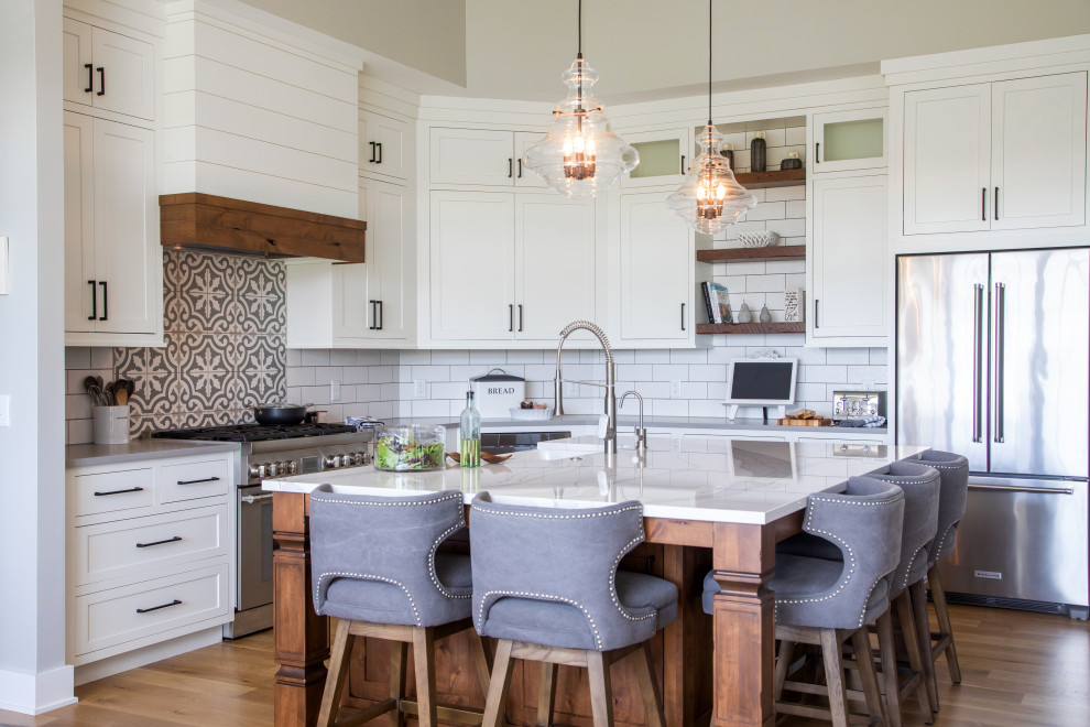 Design ideas for a large farmhouse l-shaped open plan kitchen in Milwaukee with a belfast sink, flat-panel cabinets, white cabinets, engineered stone countertops, white splashback, porcelain splashback, stainless steel appliances, dark hardwood flooring, an island and white worktops.