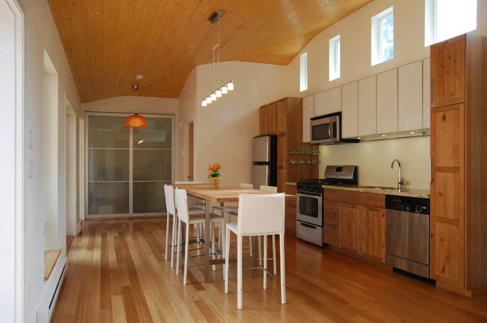 Bild på ett litet funkis linjärt kök och matrum, med en dubbel diskho, luckor med glaspanel, skåp i mellenmörkt trä, granitbänkskiva, vitt stänkskydd, stänkskydd i keramik, rostfria vitvaror, bambugolv och en köksö