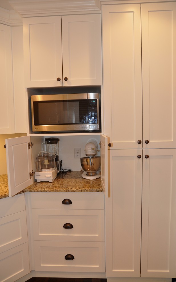 Inredning av ett modernt litet kök, med en rustik diskho, vita skåp, granitbänkskiva, rostfria vitvaror, mörkt trägolv, en halv köksö, skåp i shakerstil och brunt golv