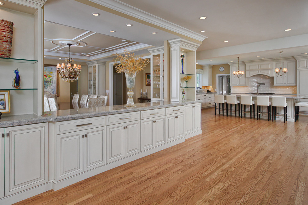 Inspiration for a large timeless l-shaped light wood floor open concept kitchen remodel in Philadelphia with an undermount sink, raised-panel cabinets, white cabinets, granite countertops, white backsplash, subway tile backsplash, stainless steel appliances and an island
