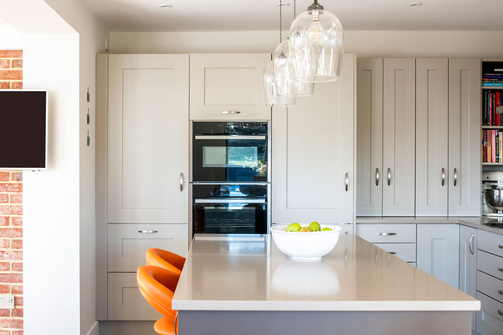 This is an example of a medium sized contemporary l-shaped open plan kitchen in Buckinghamshire with shaker cabinets, grey cabinets and an island.