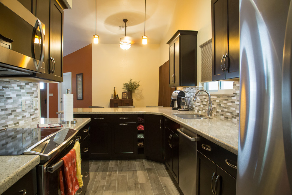 Inredning av ett klassiskt avskilt, litet u-kök, med en undermonterad diskho, luckor med upphöjd panel, skåp i mörkt trä, bänkskiva i kvartsit, grått stänkskydd, stänkskydd i mosaik, rostfria vitvaror, klinkergolv i porslin och en halv köksö