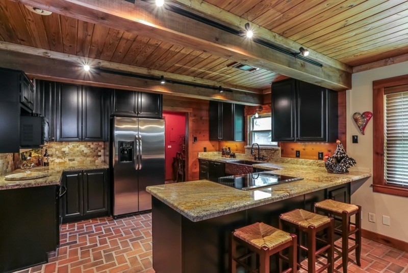 Idéer för ett kök, med en rustik diskho, luckor med upphöjd panel, svarta skåp, granitbänkskiva, stänkskydd med metallisk yta, stänkskydd i stenkakel, tegelgolv och en halv köksö