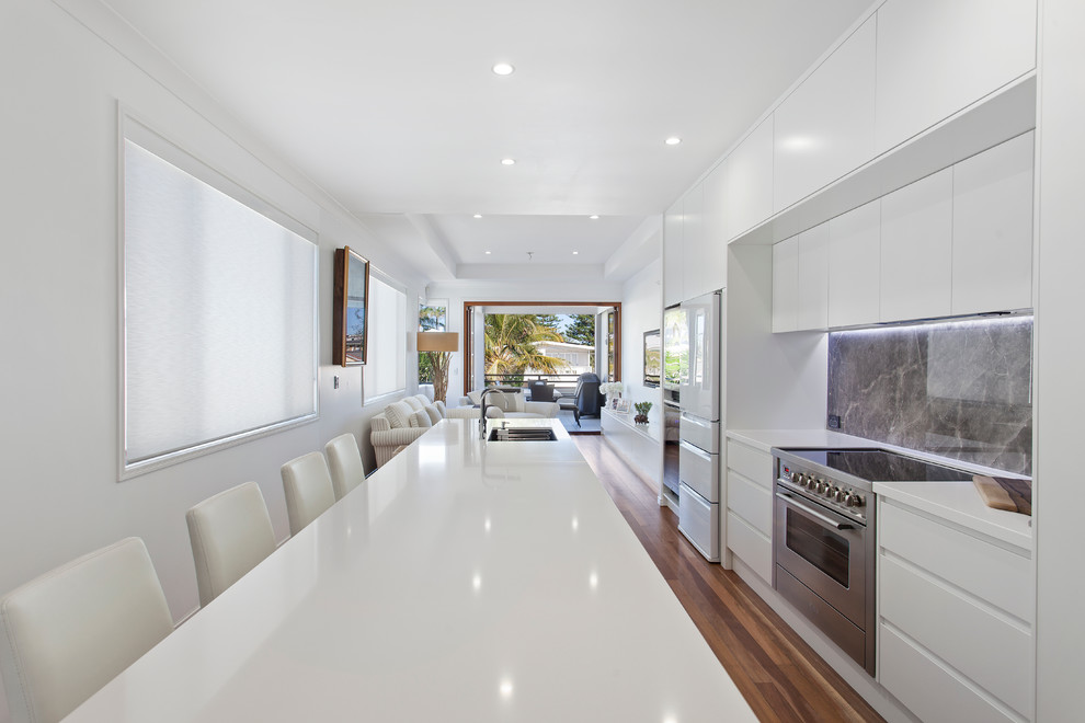 Moderne Küche mit Unterbauwaschbecken, flächenbündigen Schrankfronten, weißen Schränken, Küchenrückwand in Grau, Küchengeräten aus Edelstahl, braunem Holzboden und Kücheninsel in Brisbane