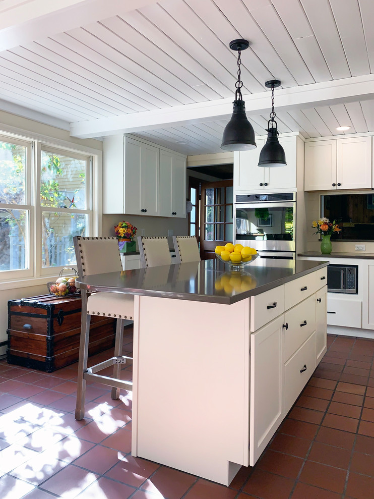 Exempel på ett mellanstort amerikanskt brun brunt kök, med en undermonterad diskho, luckor med infälld panel, vita skåp, bänkskiva i koppar, beige stänkskydd, stänkskydd i trä, rostfria vitvaror, klinkergolv i terrakotta, en köksö och rött golv