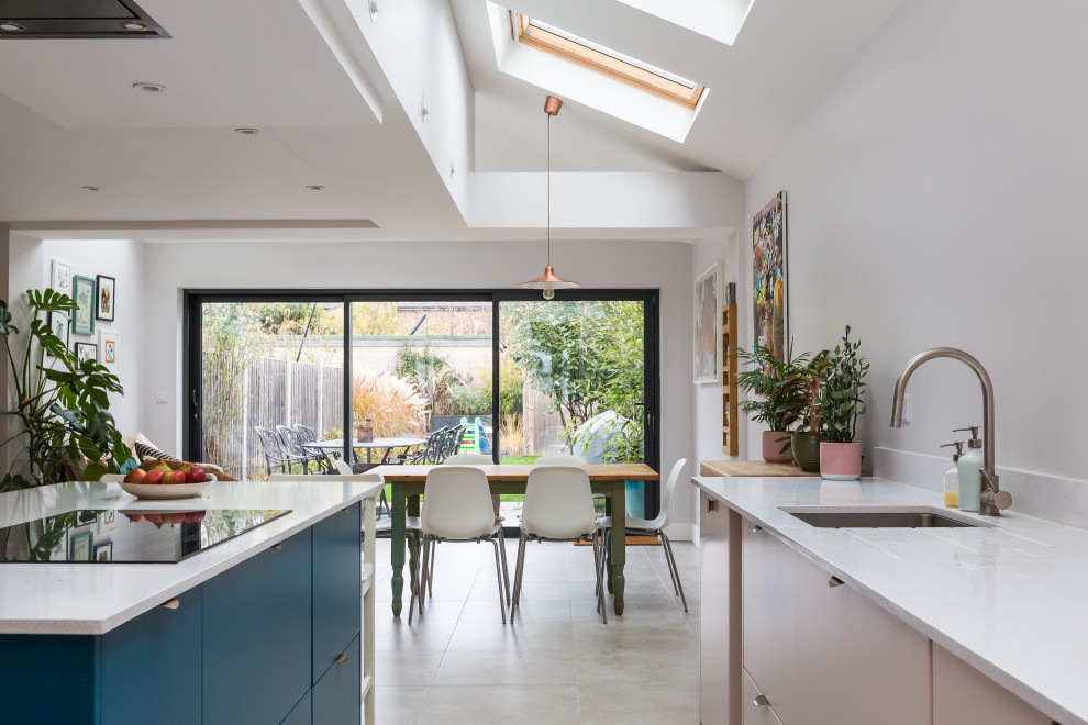 Photo of a large contemporary galley kitchen/diner in Essex with a single-bowl sink, flat-panel cabinets, blue cabinets, white splashback, an island, white worktops and beige floors.