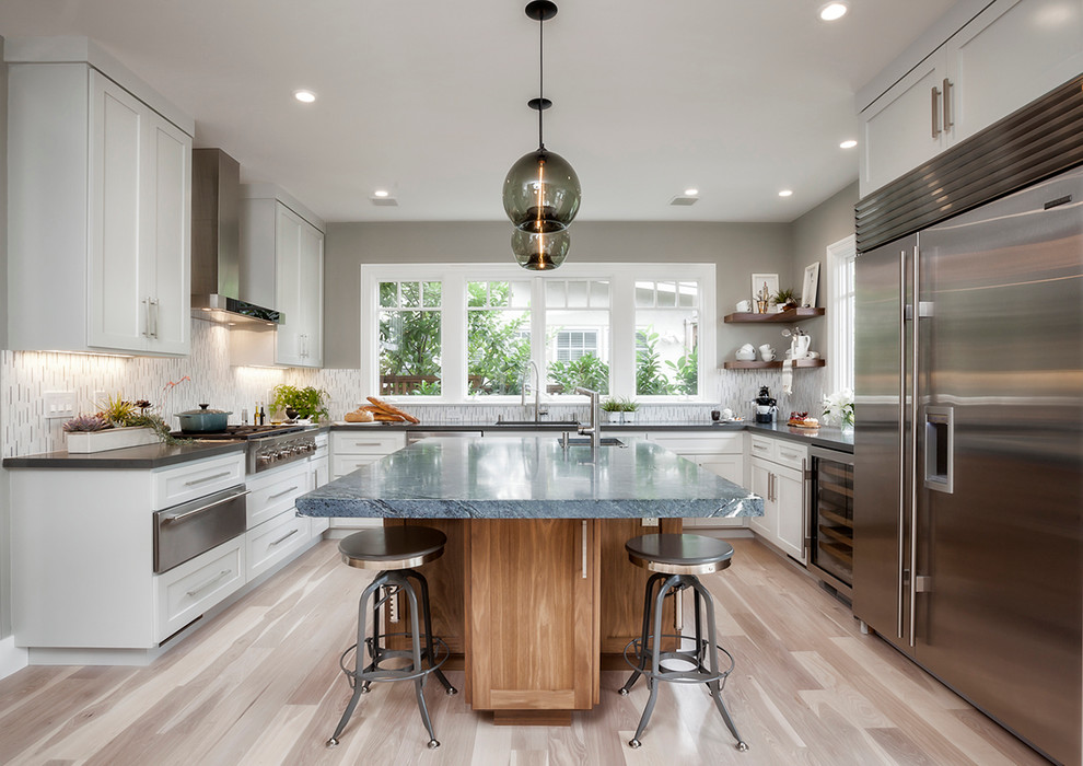 This is an example of a traditional u-shaped kitchen in San Francisco with shaker cabinets, white cabinets, white splashback, mosaic tiled splashback, stainless steel appliances, light hardwood flooring and an island.