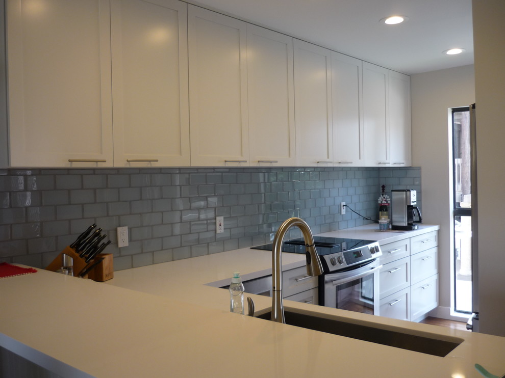 Photo of a small nautical u-shaped enclosed kitchen in Los Angeles with a single-bowl sink, shaker cabinets, white cabinets, engineered stone countertops, blue splashback, glass tiled splashback, stainless steel appliances and light hardwood flooring.