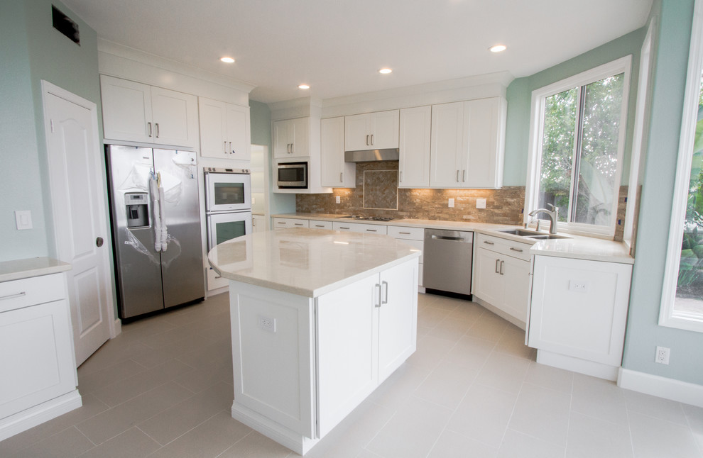 Example of a mid-sized trendy l-shaped porcelain tile and beige floor open concept kitchen design in Orange County with a double-bowl sink, shaker cabinets, white cabinets, beige backsplash, stone tile backsplash, stainless steel appliances, an island and solid surface countertops