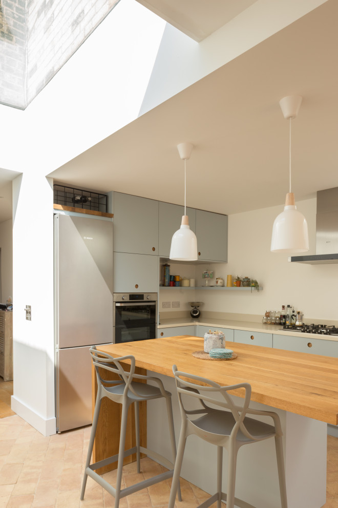 Foto på ett mellanstort funkis beige kök, med en integrerad diskho, släta luckor, blå skåp, bänkskiva i koppar, vitt stänkskydd, rostfria vitvaror, klinkergolv i terrakotta, en köksö och rosa golv