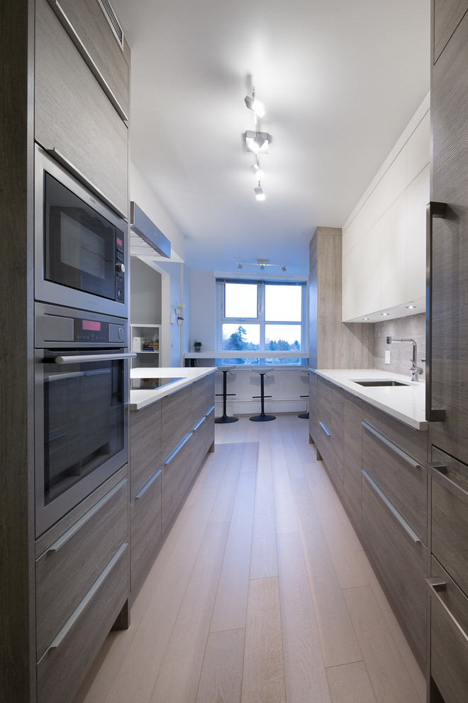 Photo of a small modern single-wall kitchen/diner in Vancouver with a submerged sink, flat-panel cabinets, light wood cabinets, quartz worktops, grey splashback, ceramic splashback, integrated appliances, light hardwood flooring and a breakfast bar.