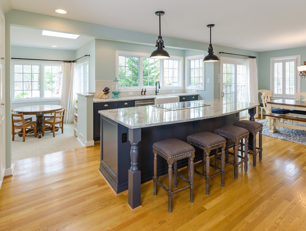 Inredning av ett klassiskt kök, med en rustik diskho, luckor med infälld panel, svarta skåp, bänkskiva i kvartsit, blått stänkskydd, rostfria vitvaror, mellanmörkt trägolv och en köksö