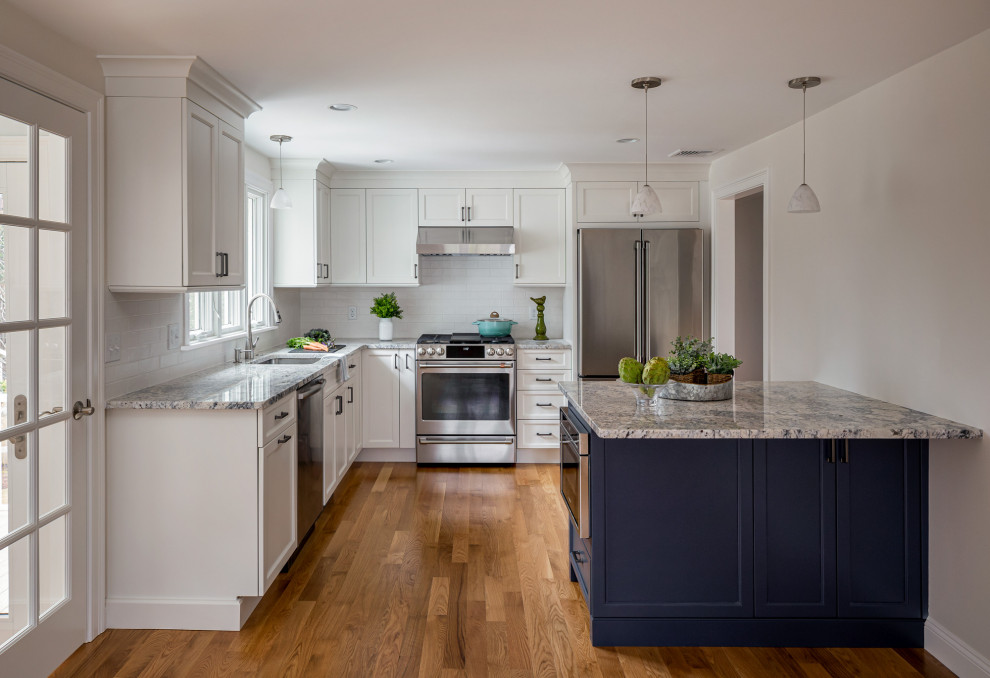 ボストンにあるお手頃価格の中くらいなトランジショナルスタイルのおしゃれなキッチン (アンダーカウンターシンク、フラットパネル扉のキャビネット、青いキャビネット、御影石カウンター、白いキッチンパネル、サブウェイタイルのキッチンパネル、シルバーの調理設備、淡色無垢フローリング、茶色い床、マルチカラーのキッチンカウンター) の写真