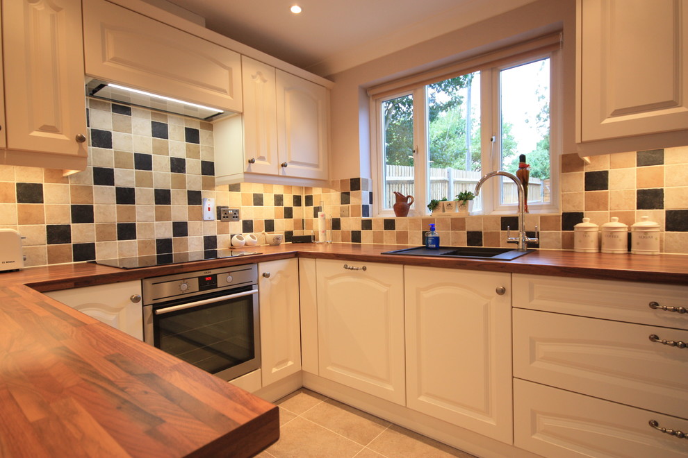 Inspiration for a medium sized country u-shaped enclosed kitchen in Kent with a built-in sink, recessed-panel cabinets, beige cabinets, wood worktops, multi-coloured splashback, ceramic splashback, stainless steel appliances, ceramic flooring and no island.