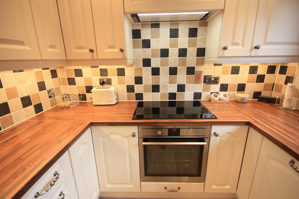 Photo of a medium sized farmhouse u-shaped enclosed kitchen in Kent with a built-in sink, recessed-panel cabinets, beige cabinets, wood worktops, multi-coloured splashback, ceramic splashback, stainless steel appliances, ceramic flooring and no island.