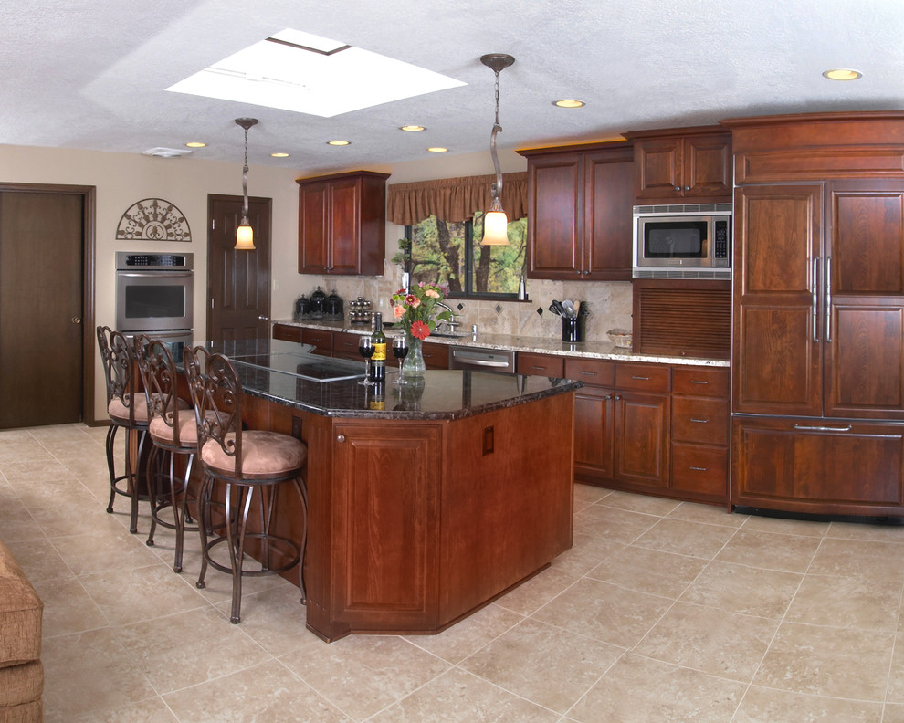 Example of a large classic single-wall laminate floor and beige floor open concept kitchen design in Albuquerque with an undermount sink, glass-front cabinets, dark wood cabinets, granite countertops, beige backsplash, stone tile backsplash, stainless steel appliances, an island and black countertops