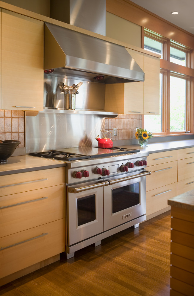 Bild på ett mellanstort funkis kök, med en undermonterad diskho, släta luckor, skåp i ljust trä, granitbänkskiva, grått stänkskydd, stänkskydd i stenkakel, rostfria vitvaror, ljust trägolv och en köksö