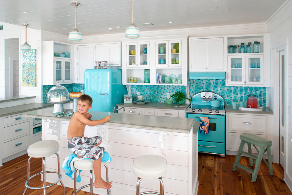Modelo de cocinas en L marinera con armarios tipo vitrina, puertas de armario blancas, encimera de cemento, salpicadero multicolor, salpicadero con mosaicos de azulejos, electrodomésticos de colores, suelo de madera en tonos medios y una isla