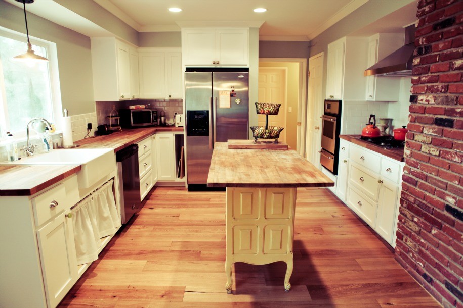 Photo of a medium sized rural u-shaped kitchen/diner in San Diego with a belfast sink, white cabinets, wood worktops, white splashback, ceramic splashback, stainless steel appliances, medium hardwood flooring and an island.