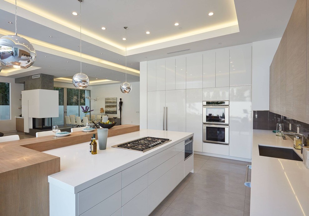 This is an example of a large contemporary u-shaped kitchen/diner in Orange County with a submerged sink, flat-panel cabinets, white cabinets, engineered stone countertops, beige splashback, porcelain splashback, integrated appliances, concrete flooring, an island, grey floors and white worktops.