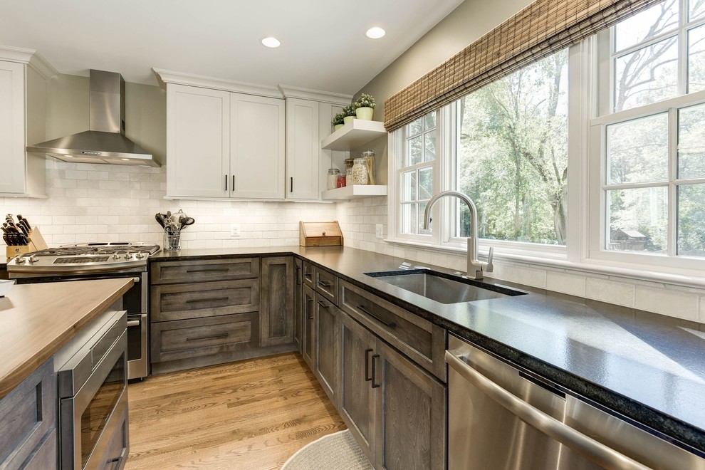 Ejemplo de cocinas en L clásica renovada de tamaño medio cerrada con fregadero bajoencimera, armarios estilo shaker, puertas de armario de madera en tonos medios, encimera de esteatita, salpicadero beige, salpicadero de azulejos de piedra, electrodomésticos de acero inoxidable, suelo de madera clara, una isla y suelo marrón