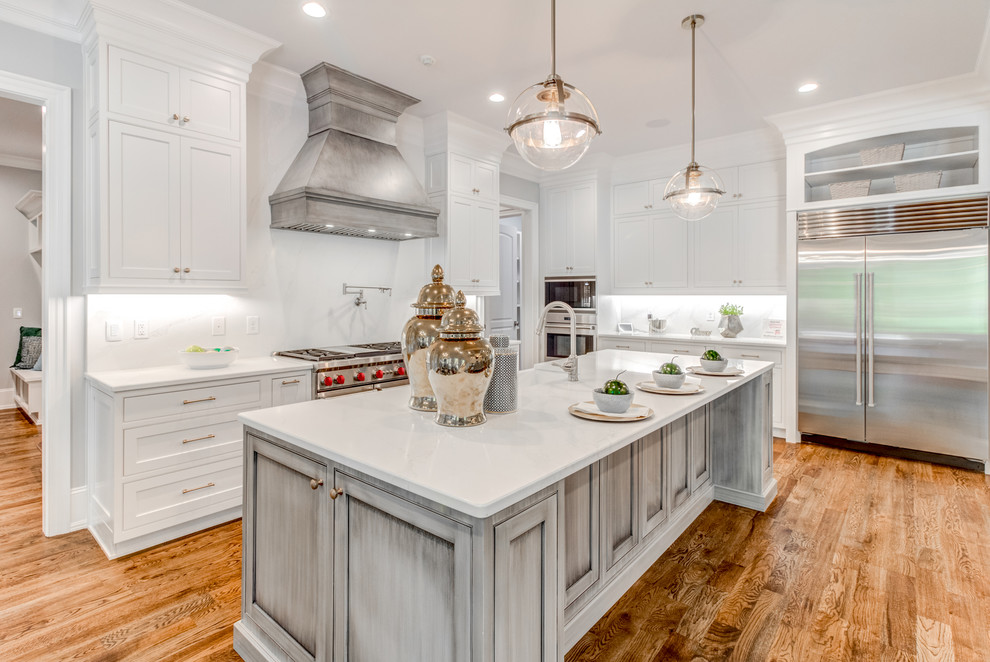 Bild på ett vintage vit vitt kök, med en rustik diskho, luckor med profilerade fronter, grå skåp, bänkskiva i kvarts, vitt stänkskydd, rostfria vitvaror, mellanmörkt trägolv, en köksö och brunt golv