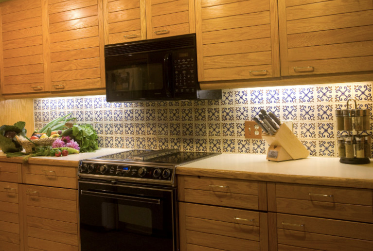 Cette image montre une petite cuisine américaine parallèle sud-ouest américain avec un placard à porte shaker, des portes de placard blanches, un plan de travail en surface solide, une crédence bleue, une crédence en céramique, un électroménager noir, parquet en bambou et un sol beige.