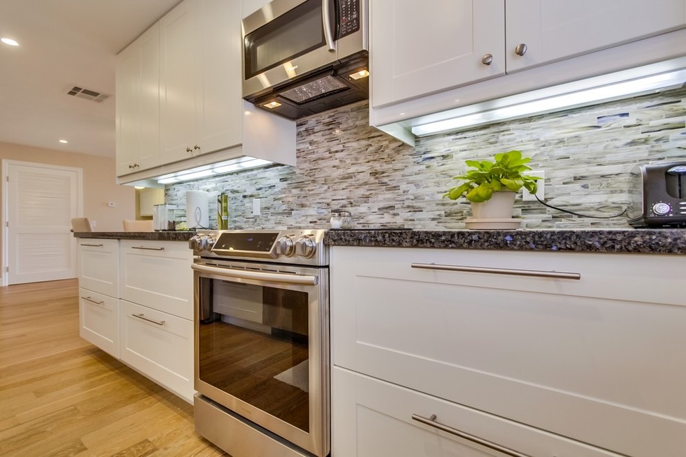 Photo of a medium sized traditional galley enclosed kitchen in Los Angeles with a submerged sink, shaker cabinets, white cabinets, granite worktops, multi-coloured splashback, stainless steel appliances, matchstick tiled splashback, medium hardwood flooring and no island.