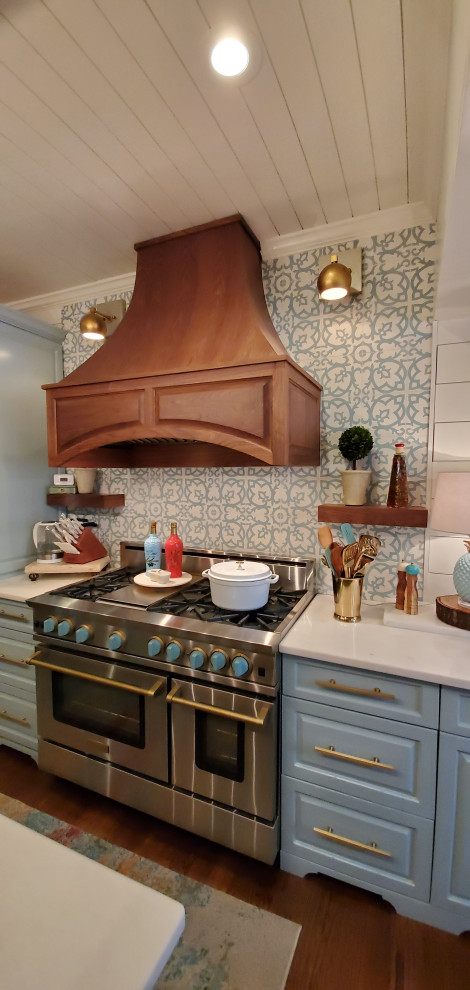 Cette image montre une cuisine américaine linéaire bohème de taille moyenne avec plan de travail en marbre, une crédence bleue, une crédence en carreau de ciment, un électroménager en acier inoxydable, un sol en bois brun, îlot et un plan de travail blanc.