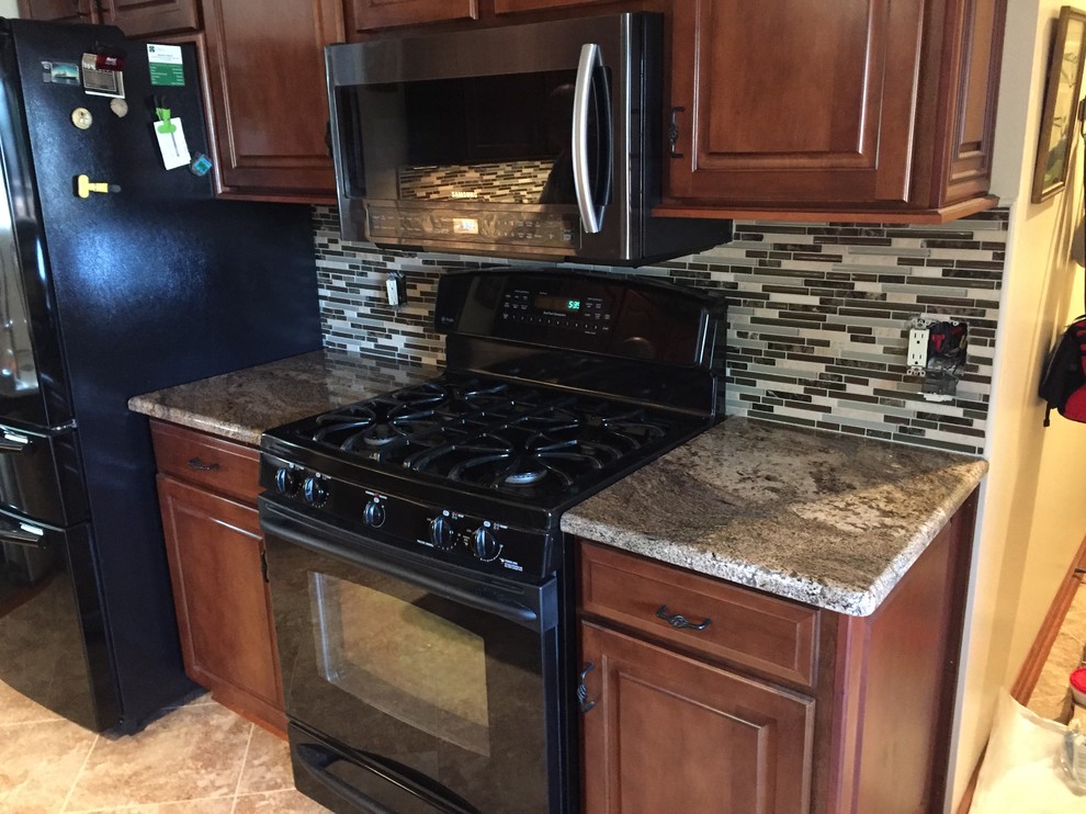 Example of a mid-sized classic single-wall travertine floor and brown floor enclosed kitchen design in Other with raised-panel cabinets, dark wood cabinets, granite countertops, multicolored backsplash, matchstick tile backsplash, black appliances and no island