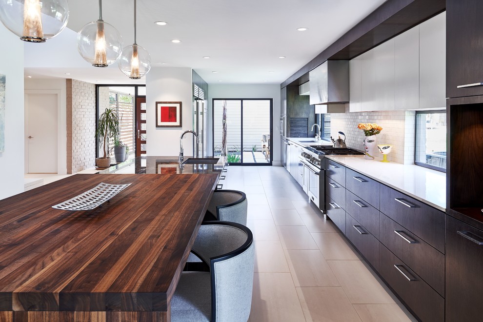 Eat-in kitchen - mid-sized contemporary galley ceramic tile eat-in kitchen idea in Houston with a single-bowl sink, flat-panel cabinets, dark wood cabinets, wood countertops, white backsplash, subway tile backsplash, stainless steel appliances and an island