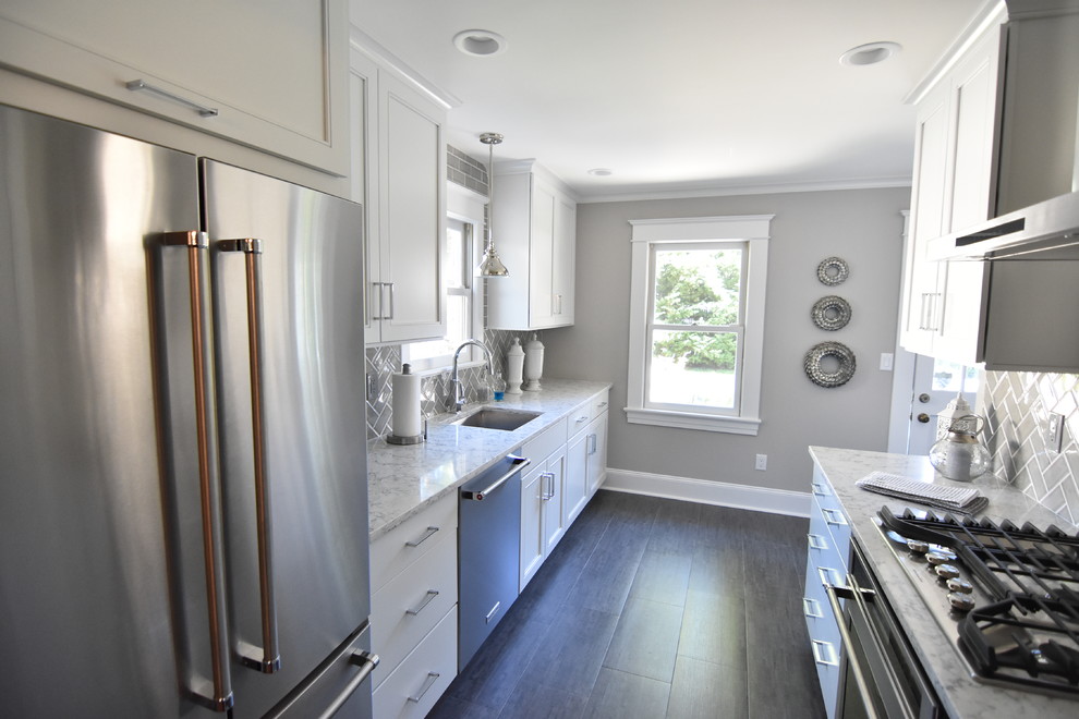 This is an example of a traditional galley enclosed kitchen in New York with a single-bowl sink, shaker cabinets, white cabinets, marble worktops, grey splashback, metro tiled splashback, stainless steel appliances, dark hardwood flooring, no island and brown floors.